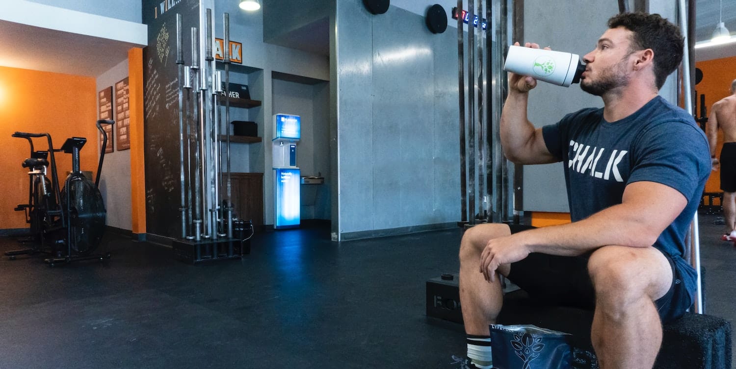 man drinks a protein shake inside of a gym