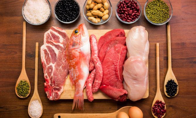 Several high-quality protein options laid on a butcher's block, including beef, fish, chicken, eggs and legumes.