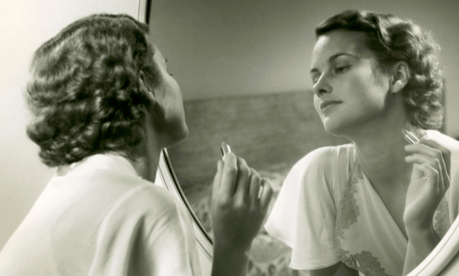 woman looking in mirror and putting on lipstick